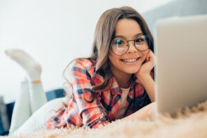Mirthful teenager wearing glasses lying on the bed