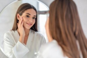 Young Female Smiling To Her Reflection In Mirror, Beautiful Millennial Woman Enjoying Her Appearance